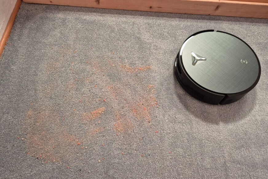 ECOVACS X12 OMNICYCLONE saugt Sand von einem grauen Kurzflorteppich
